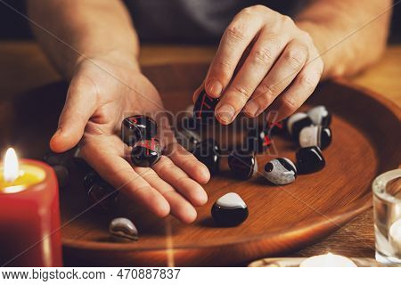 Man's Hand Holds A Rune Of Fehu With Fingers. He Shows Runes On Another Hand. There Are Stones With 