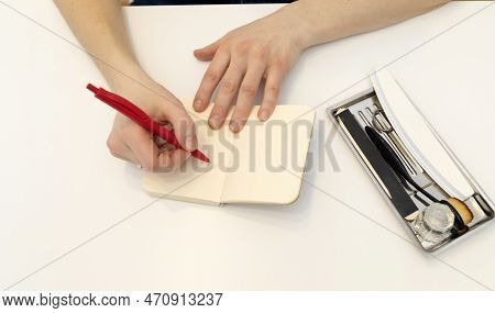 Unrecognizable Nail Master Makes Notes In Notebook With Pen, Sitting At Workstation, Able In Nail Be