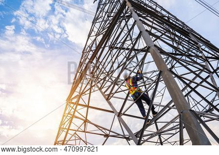 A Workers Wearing Safety Harnesses Climb High-voltage Pylons For Inspection And Maintenance At A Hig