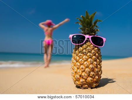 Cheerful pineapple glasses and a woman in a bikini sunbathing on the beach on sea background. Ideali