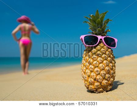 Cheerful pineapple glasses and a woman in a bikini sunbathing on the beach on sea background. Ideali