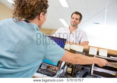 Rear view of nurse assisting man while working at reception desk in hospital