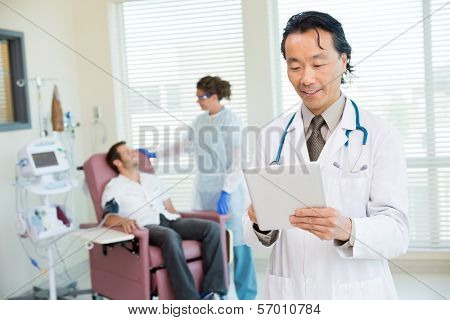Portrait of male doctor with nurse and chemo patient in background.