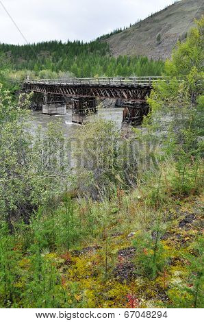 Wooden Bridge In Yakutia Across The Mountain River.