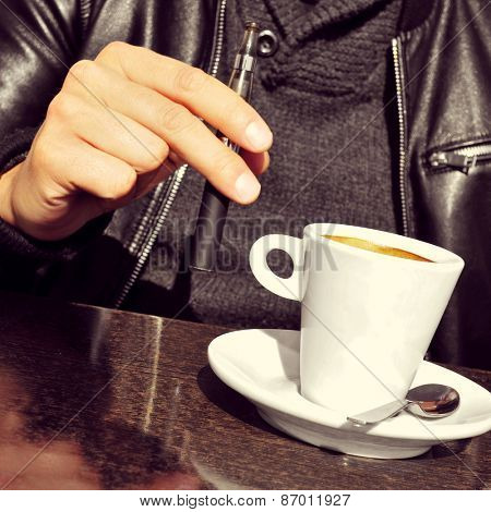 closeup of a young man with an electronic cigarette and a cup of coffee in the terrace of a cafe
