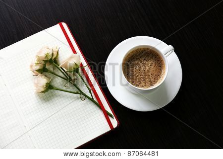 Cup of coffee with notebook and fresh flower on wooden table background