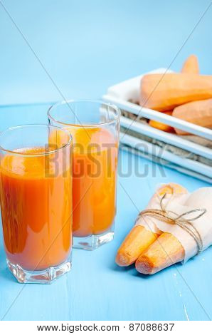 Freshly squeezed carrot juice in the glasses.A box with purified carrot on a blue wooden background.