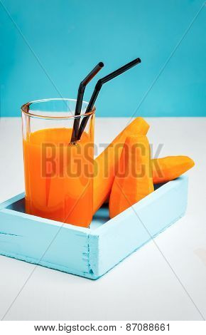 Freshly squeezed carrot juice in the glasses.A box with purified carrot on a blue wooden background.