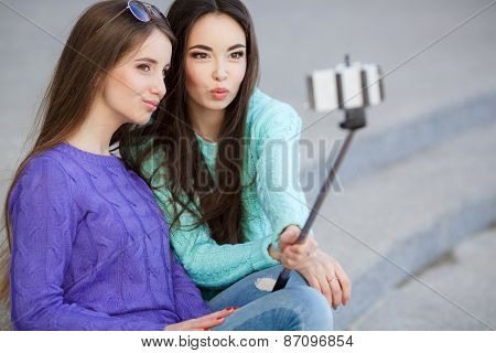 Two young attractive women are photographed with a smartphone on the streets.