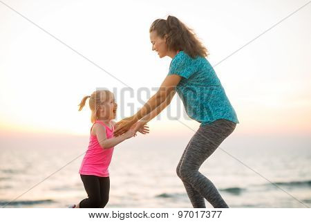 Fit Young Mother And Daughter Playing On The Beach At Sunset