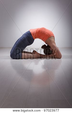 Beautiful sporty fit yogini woman practices yoga asana Kapotasana - pigeon pose intense backbend in studio