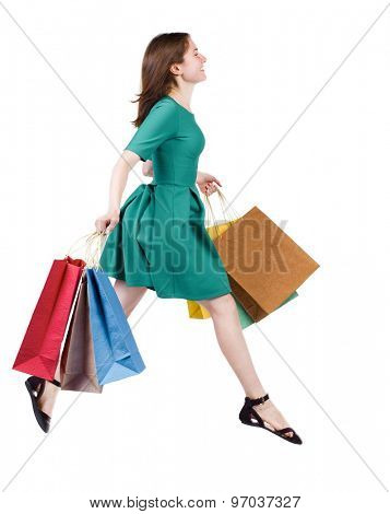 side view of a woman jumping with shopping bags. beautiful brunette girl in motion.   Isolated over white background. The girl in stylish green dress ambled happily flying with shopping bags.