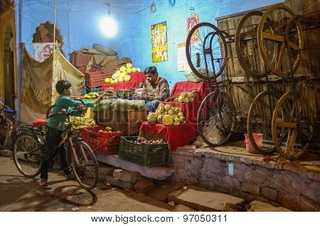 JODHPUR, INDIA - 07 FEBRUARY 2015: Grocery store next to wooden trolleys on big wheels used for transport of goods with store owner and young boy on bicycle.