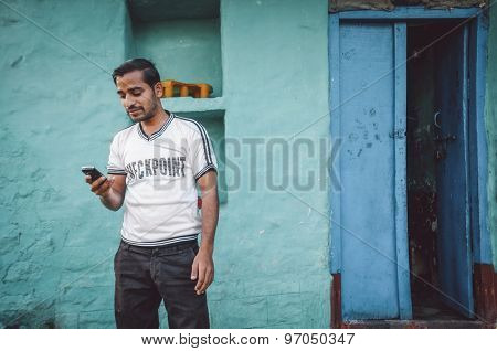 KAMALAPURAM, INDIA - 02 FABRUARY 2015: Indian man looks at his mobile phone outside his home. Post-processed with grain, texture and colour effect.