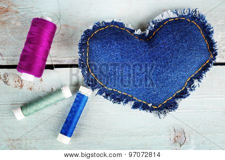 Denim heart and thread on wooden background