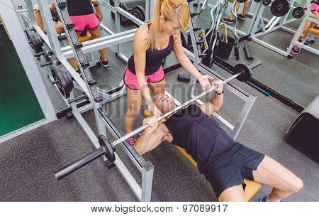 Woman coach helping to man in bench press training