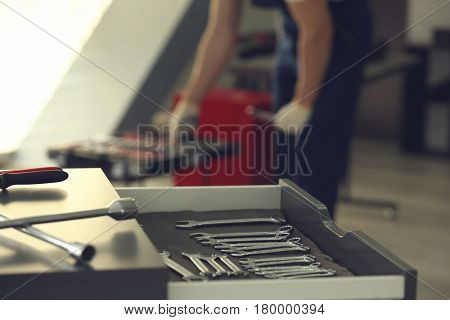 Drawer unit with tools in car repair shop and blurred auto mechanic on background