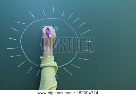 Kid drawing happy face to the greenboard with chalk