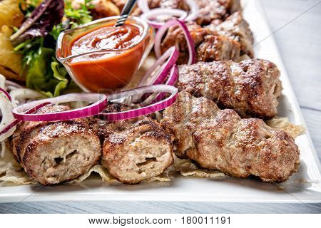 Lyulya kebab with red sauce and onion on white plate close up with selective focus.