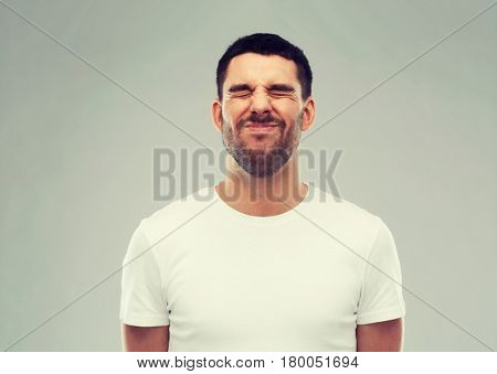 emotion and people concept - young wrying man over gray background