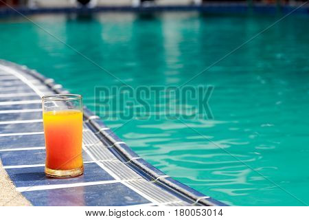 Closeup of orange juice glass standing on border of water pool