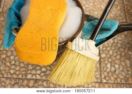 Bucket with water and soap. Sponge is in foreground and rights is broom dustpan and rag. Left on the bucket is hung rag.