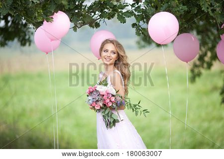 Happy beautiful young bride in a tender pink dress with a wedding bouquet in hands on a nature background