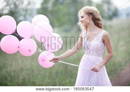 Beautiful young girl in a pink dress with balloons in hands on a nature background