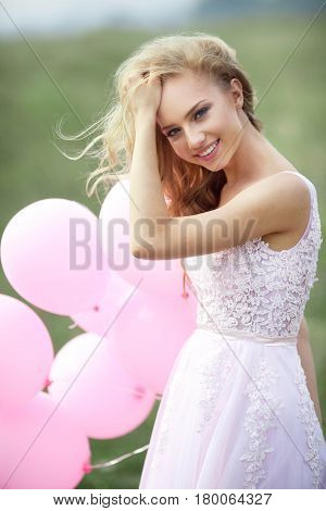 Beautiful young girl in light pink dress with balloons in hands
