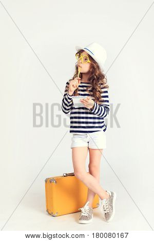 Young serious lady is thinking  and focusing on something. She is standing by her suitcase. The picture is taken at studio and has white background