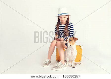 Young nice girl is sitting on a yellow suitcase and listening to music through earphones on smartphone. There is also a dog Jack-Rassel terrier next to her. Travel, tourism, vacation, listening music concept