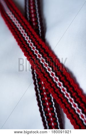 Two crossed narrow woven tapes in with ethnic pattern in red purple black and white