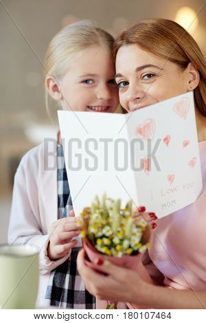 Cheerful woman anad her little daughter peeking out of open greeting-card