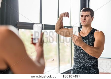 Portrait of proud bodybuilder boasting his arm muscles taking selfie in gym  mirror flexing biceps after working out