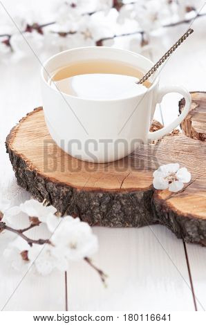 White cup of hot tea with spring flowers on a light wooden background. Herbal tea Lifestyle Spring Breakfast Light background with flowers.
