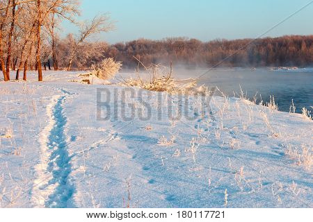 The river bank is covered with snow in which the trgopinka is trodden. Water of the river soars from a frost and branches of trees are covered with hoarfrost.