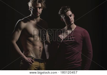 Two handsome men posing on black background. Male model in dark red tshirt with long sleeves casual wear. Muscular macho unshaven caucasian with muscle torso with six packs and abs biceps triceps