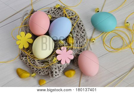 Knitted nest with Easter eggs. Thread and yellow beads with stones on a wooden background.