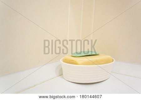 Close up of pieces of green and yellow soap in white plastic soap-dish in bathroom