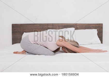 Young woman sitting on bed practice yoga pose