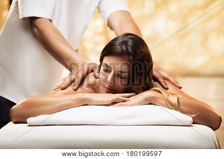 The beautiful young girl relaxes in a spa salon and gets massage