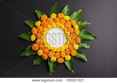 flower rangoli made using marigold or zendu flowers and mango leaves over black background with copy space in the middle, selective focus