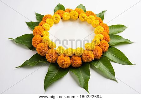 flower rangoli made using marigold or zendu flowers and mango leaves over black background with copy space in the middle, selective focus
