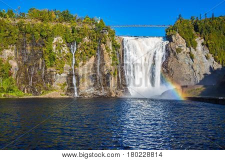 Magnificent rainbow in the waterfall Montmorency in Montmorency Falls Park, in Quebec.  Above the waterfall built bridge for walking. The concept of active and cultural tourism