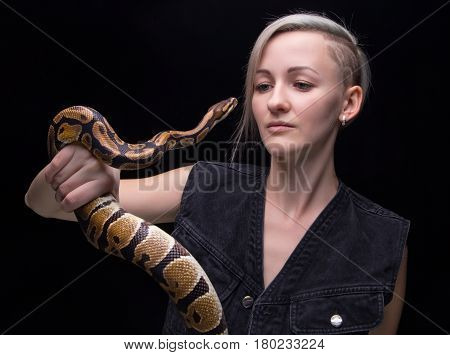Portrait of blond woman holding snake on black background