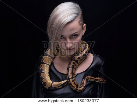 Woman in leather dress and ball python on black background