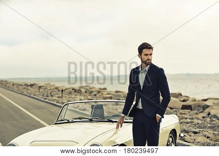 Suited dude with vintage car on road looking away