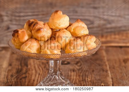Sweet cream puffs in glass tray on wooden table.