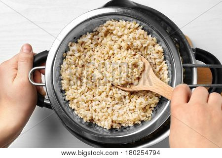 Hand with spoon stirring brown rice in colander on kitchen table