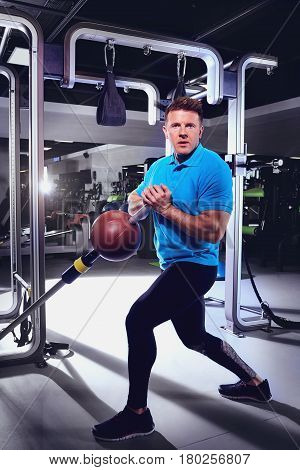 A sporty blond man doing exercises with  ball in the gym.